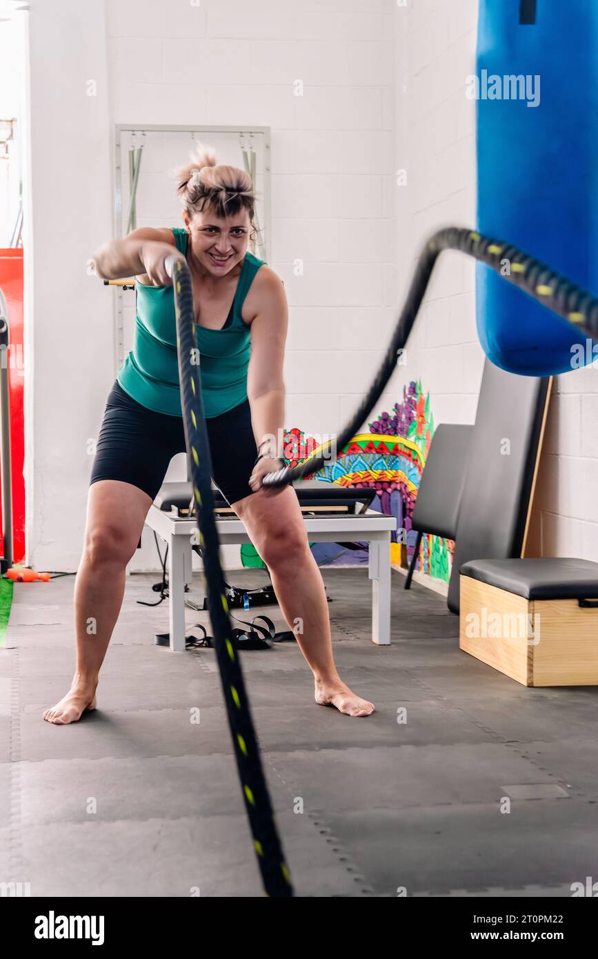 La femme fait son maximum dans un exercice de cordes de combat, démontrant son dévouement et sa détermination dans son entraînement physique dans la salle de gym. Banque D'Images