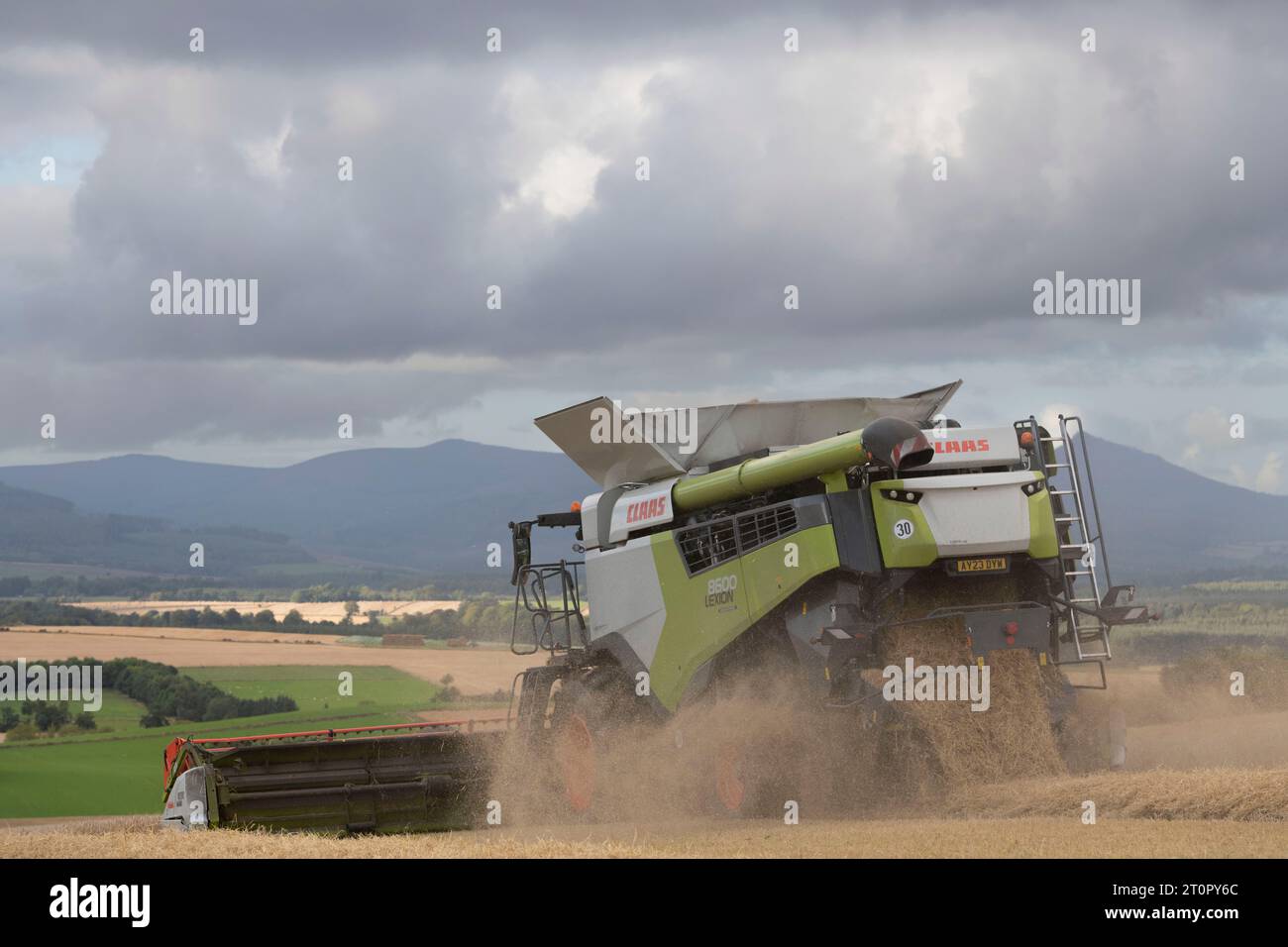 Une moissonneuse-batteuse Claas Lexion vue de derrière dans nuages de débris travaillant dans un champ d'orge Hillside avec vue sur Aberdeenshire Banque D'Images