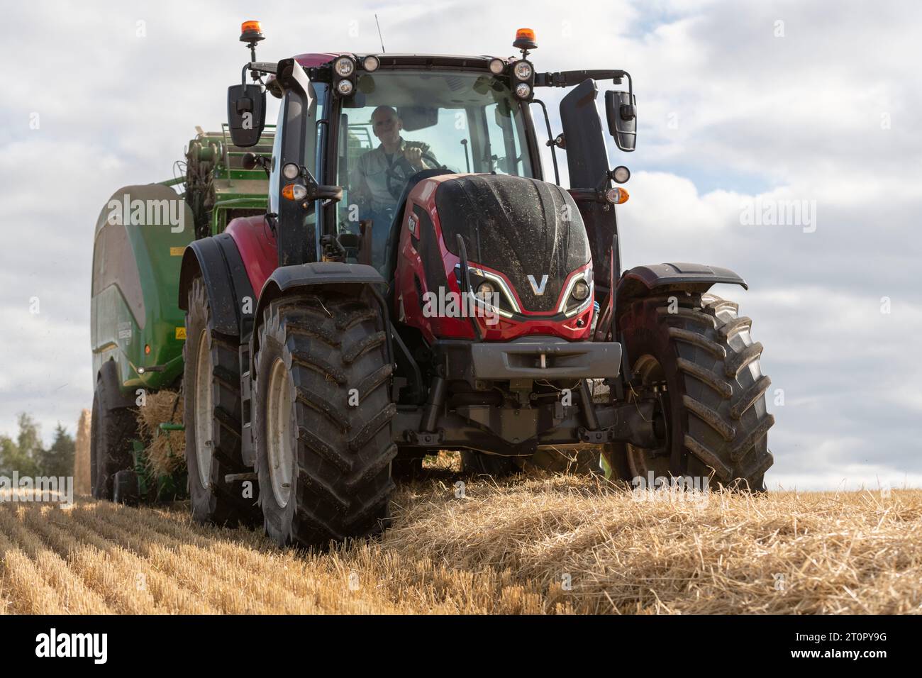Tracteur Valtra t195 rouge remorquant une ramasseuse-presse dans un champ de paille d'orge vu de l'avant et d'un point de vue bas Banque D'Images
