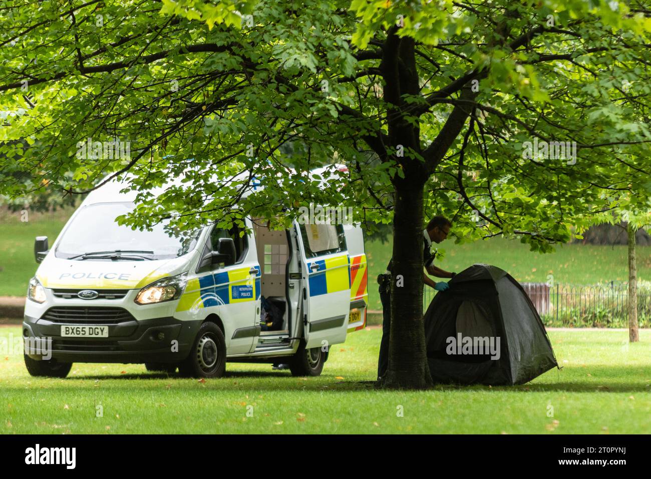 Agent de police enlevant la tente d'un dormeur rude de St James's Park, Westminster, Londres, Royaume-Uni Banque D'Images