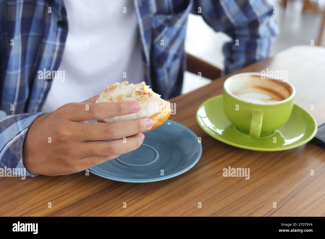Gros plan de la main masculine mangeant un beignet sucré dans le café Banque D'Images