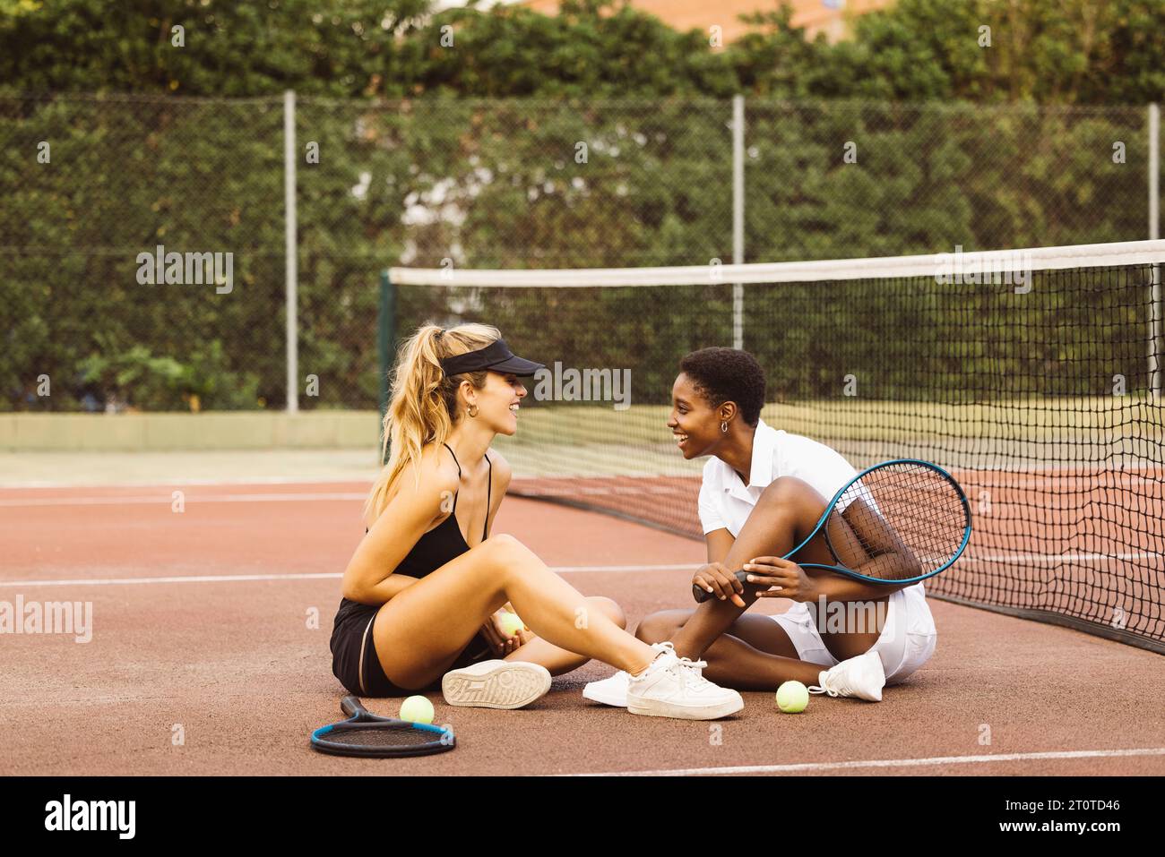 Deux jeunes belles femmes ayant une conversation assise sur un court de tennis à côté du filet. Deux joueurs de tennis amateurs faisant une pause pendant un tennis Banque D'Images