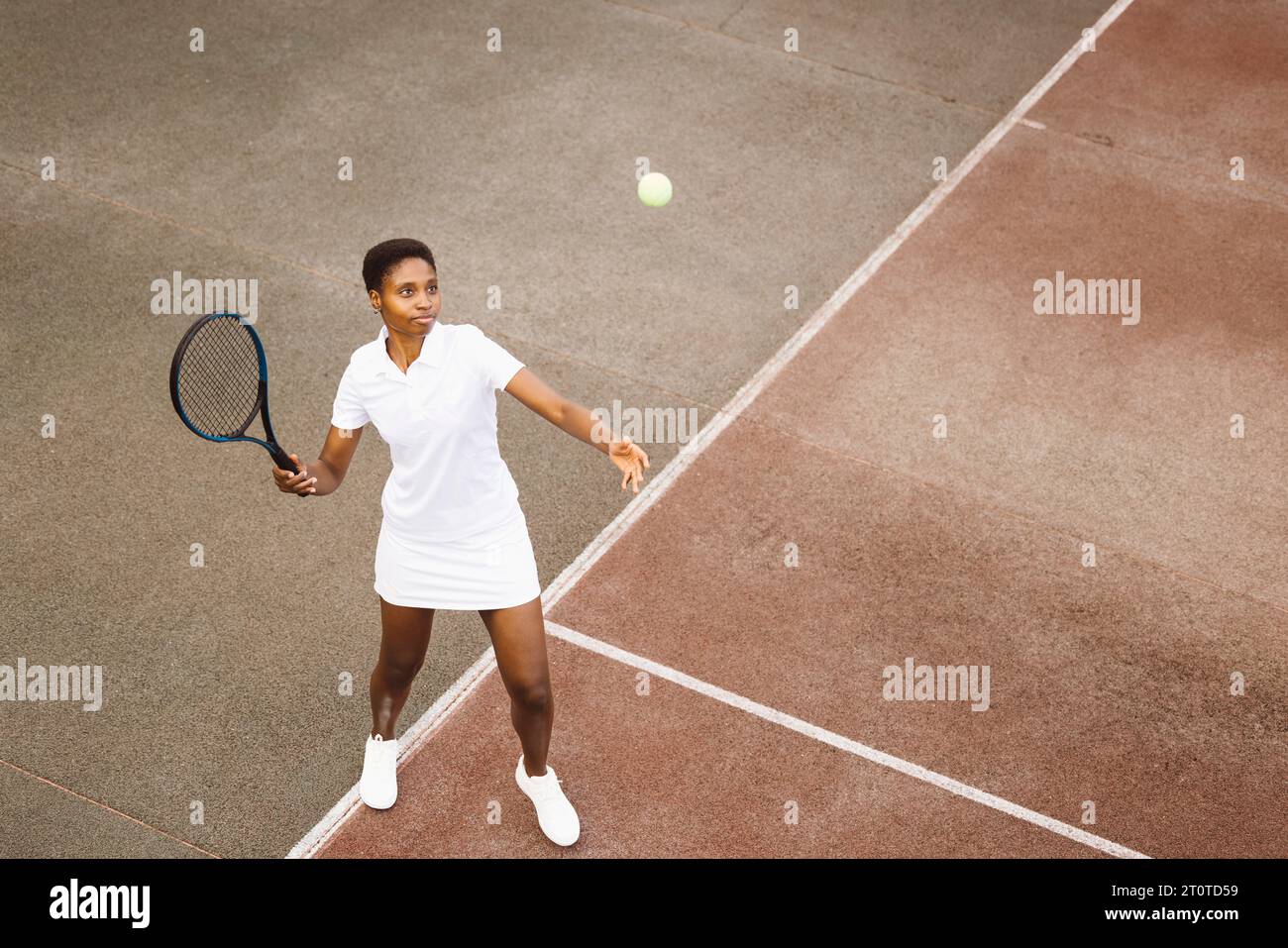 Jeune belle femme jouant un match de tennis. Femme de sport frappant un service sur un court de tennis extérieur. Banque D'Images