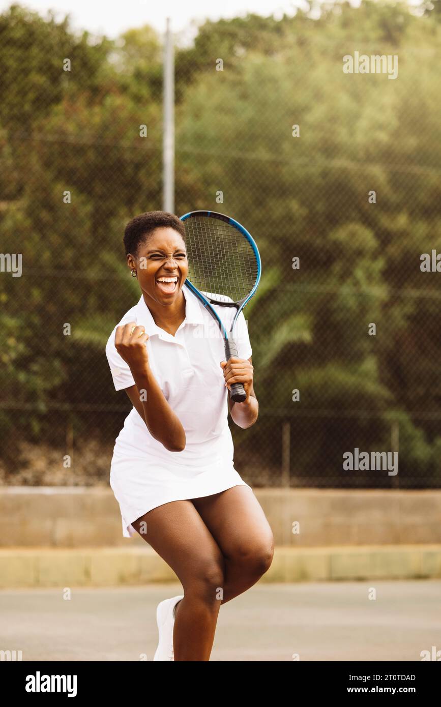 Expression effusive d'une jeune belle femme célébrant un point lors d'une partie de tennis. Femme heureuse jouant un jeu de tennis avec des amis. Banque D'Images