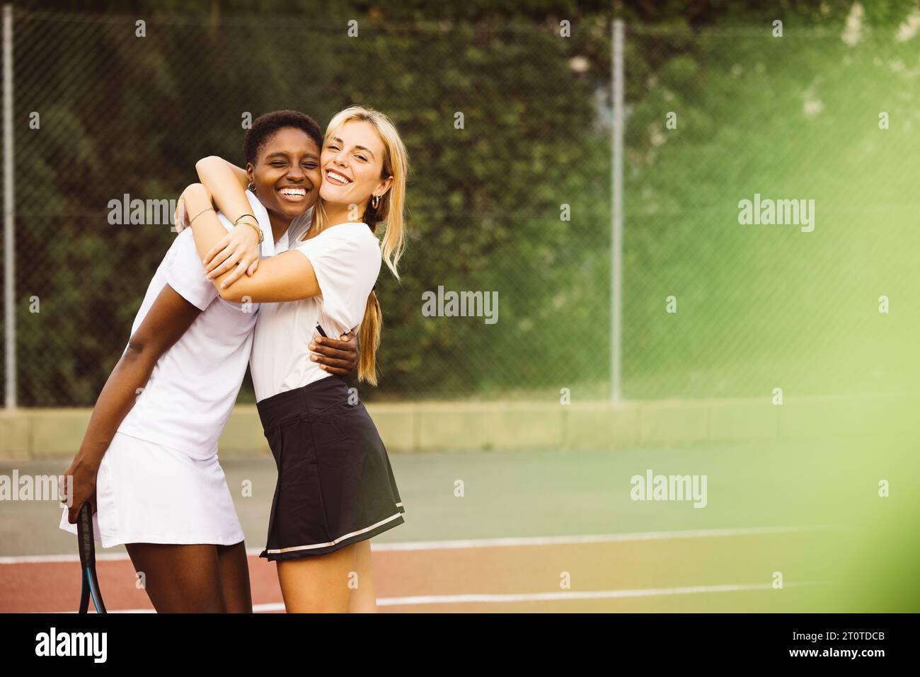Portrait de deux belles jeunes femmes heureuses avec des vêtements de tennis et des raquettes dans un court de tennis prêt à jouer un jeu. Deux amis partageant une matinée de s. Banque D'Images