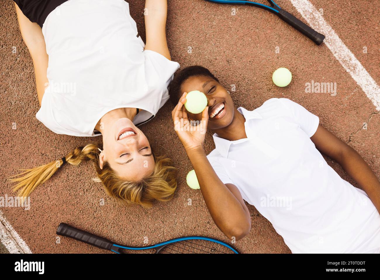 Portrait de deux jeunes femmes joueuses belles avec des vêtements de tennis et des raquettes allongées sur un court de tennis. Deux amis partageant une matinée d'acti sportifs Banque D'Images