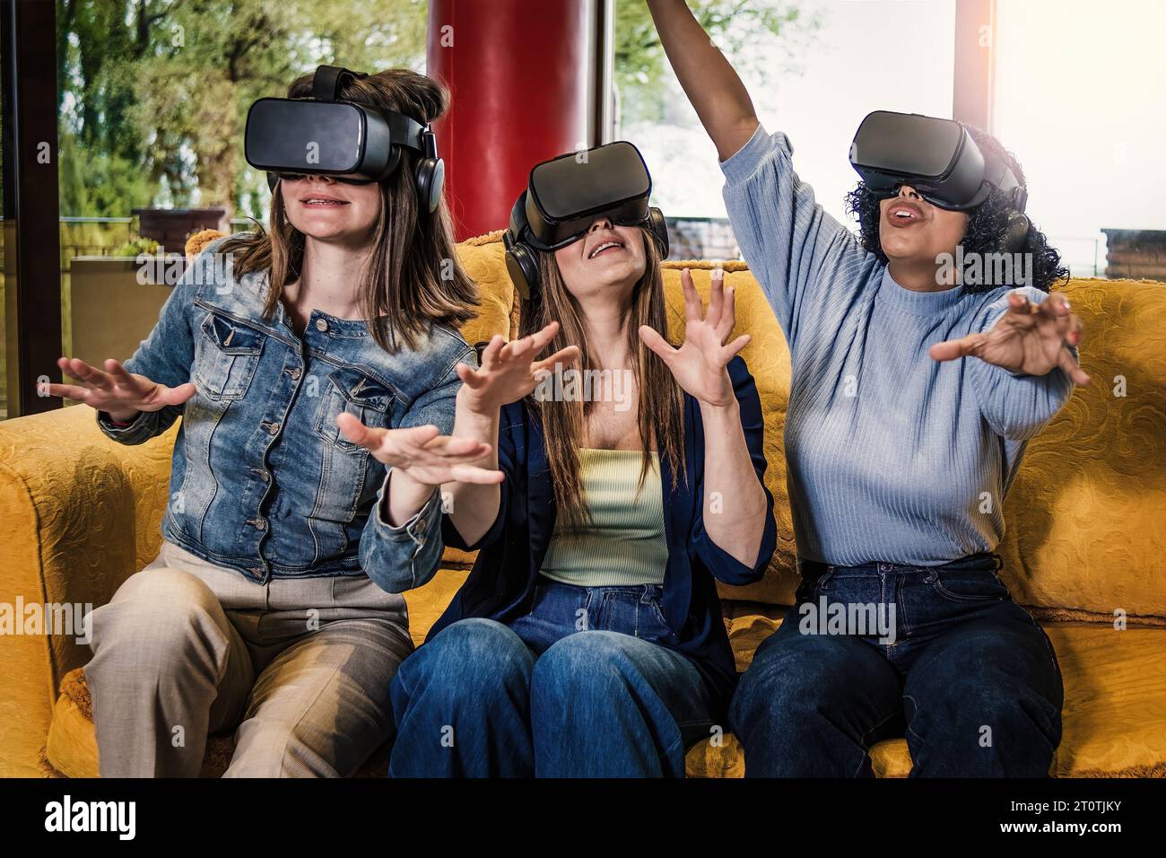Trois jeunes femmes, deux caucasiennes et une brésilienne, assises sur un canapé, ont vécu une expérience de réalité augmentée 360° 3D, en faisant des gestes de la main avec V. Banque D'Images