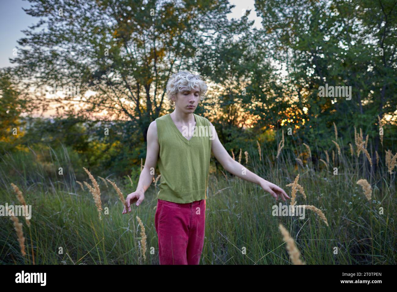 un jeune homme aux yeux fermés marche parmi l'herbe Banque D'Images