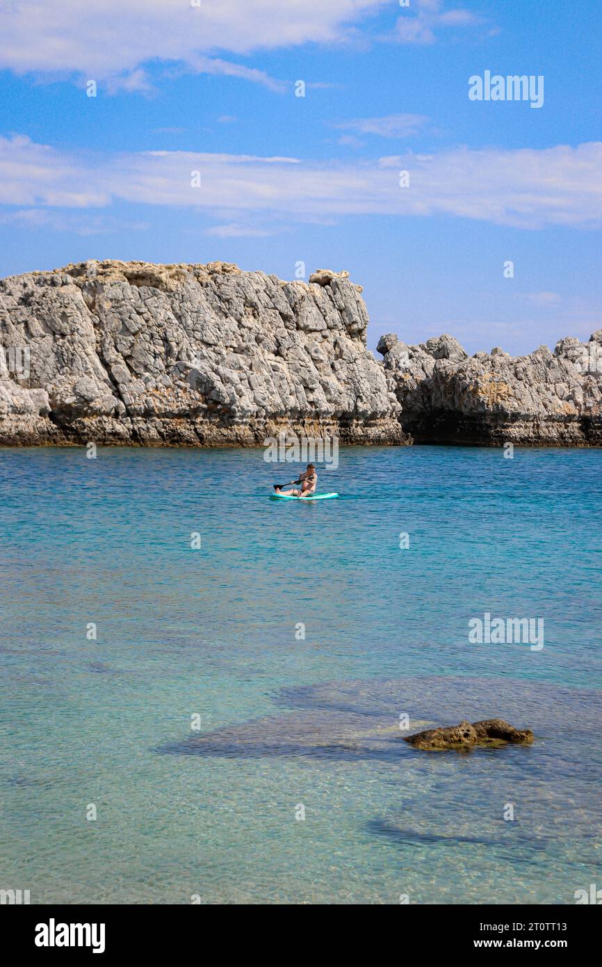 Homme célibataire assis sur une planche de surf bleu sarcelle dans l'eau de la plage de Saint Paul's Bay Banque D'Images