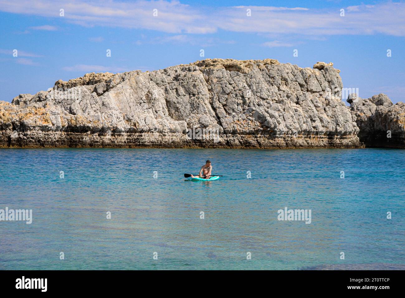 Homme célibataire assis sur une planche de surf bleu sarcelle dans l'eau de la plage de Saint Paul's Bay Banque D'Images