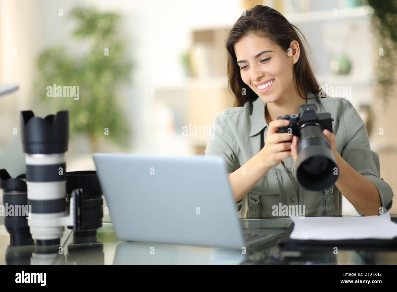 Heureux photographe vérifiant le travail sur ordinateur portable tenant l'appareil photo à la maison Banque D'Images