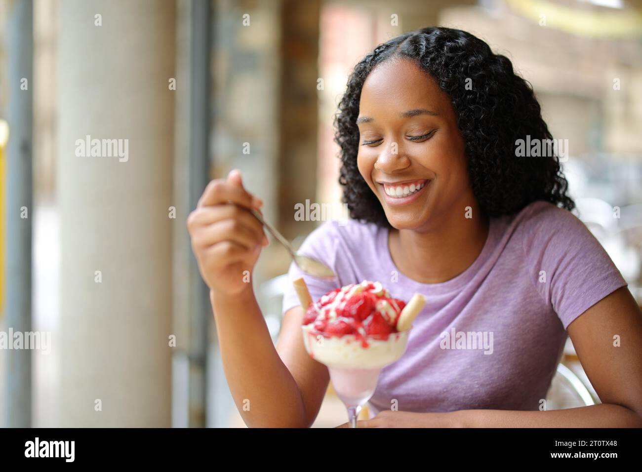 Heureuse femme noire mangeant de la crème glacée dans une terrasse de restaurant Banque D'Images