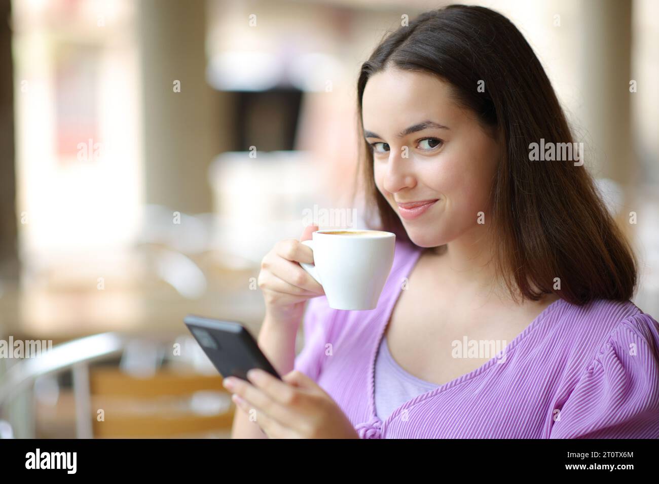 Femme buvant du café tenant le téléphone vous regardant dans une terrasse de bar Banque D'Images