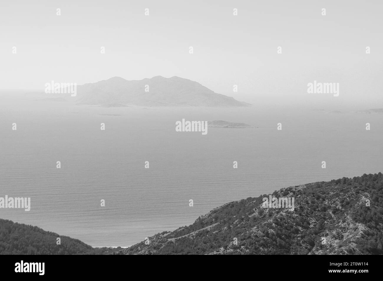 Vue côtière en noir et blanc d'une île Makri, l'une des Echinades, dans le groupe des îles Ioniennes vu de l'île de Rhodes Banque D'Images