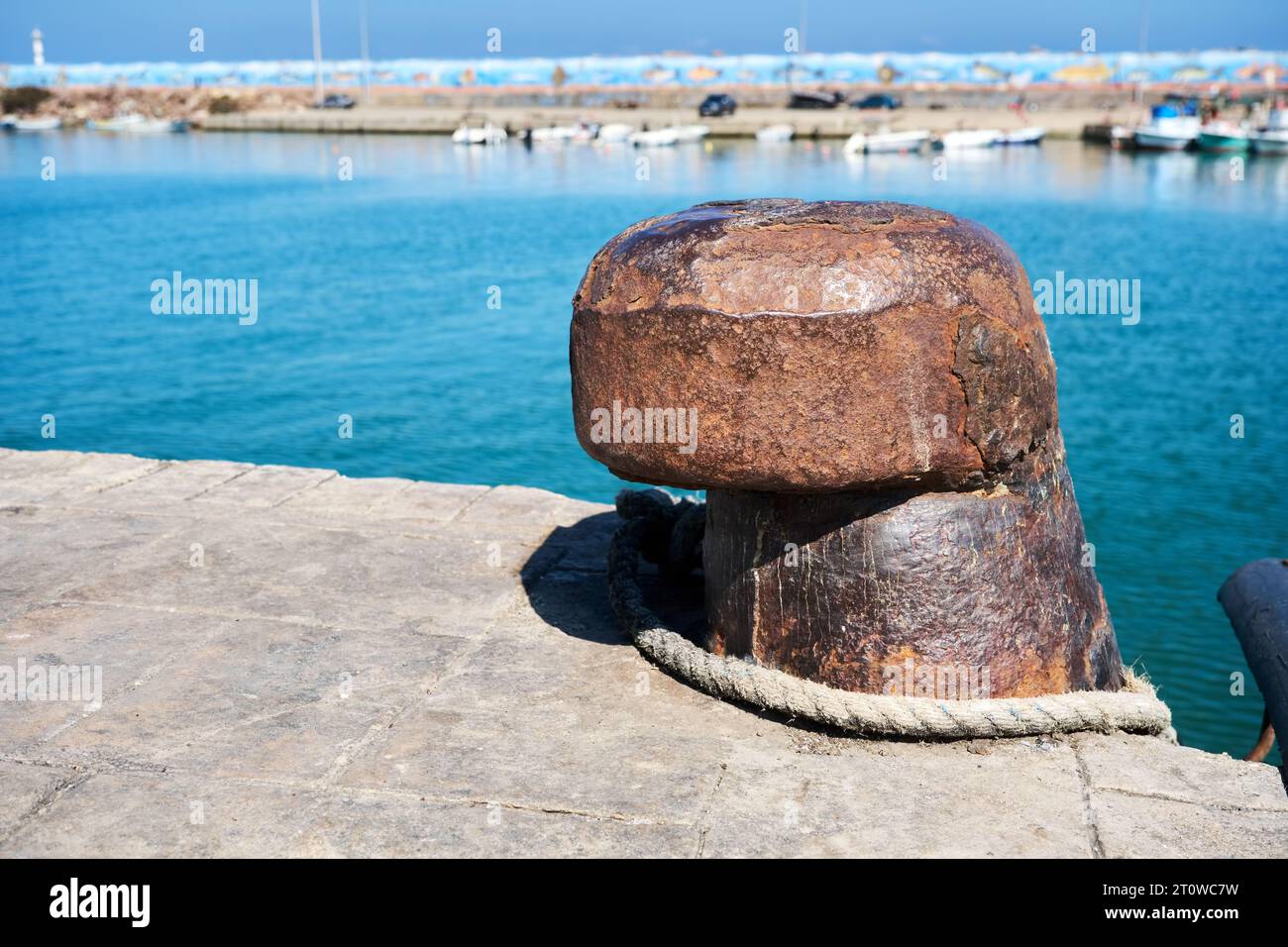 Vieux bollard d'amarrage en acier rouillé avec fond de bateaux de mer et de pêche. Banque D'Images