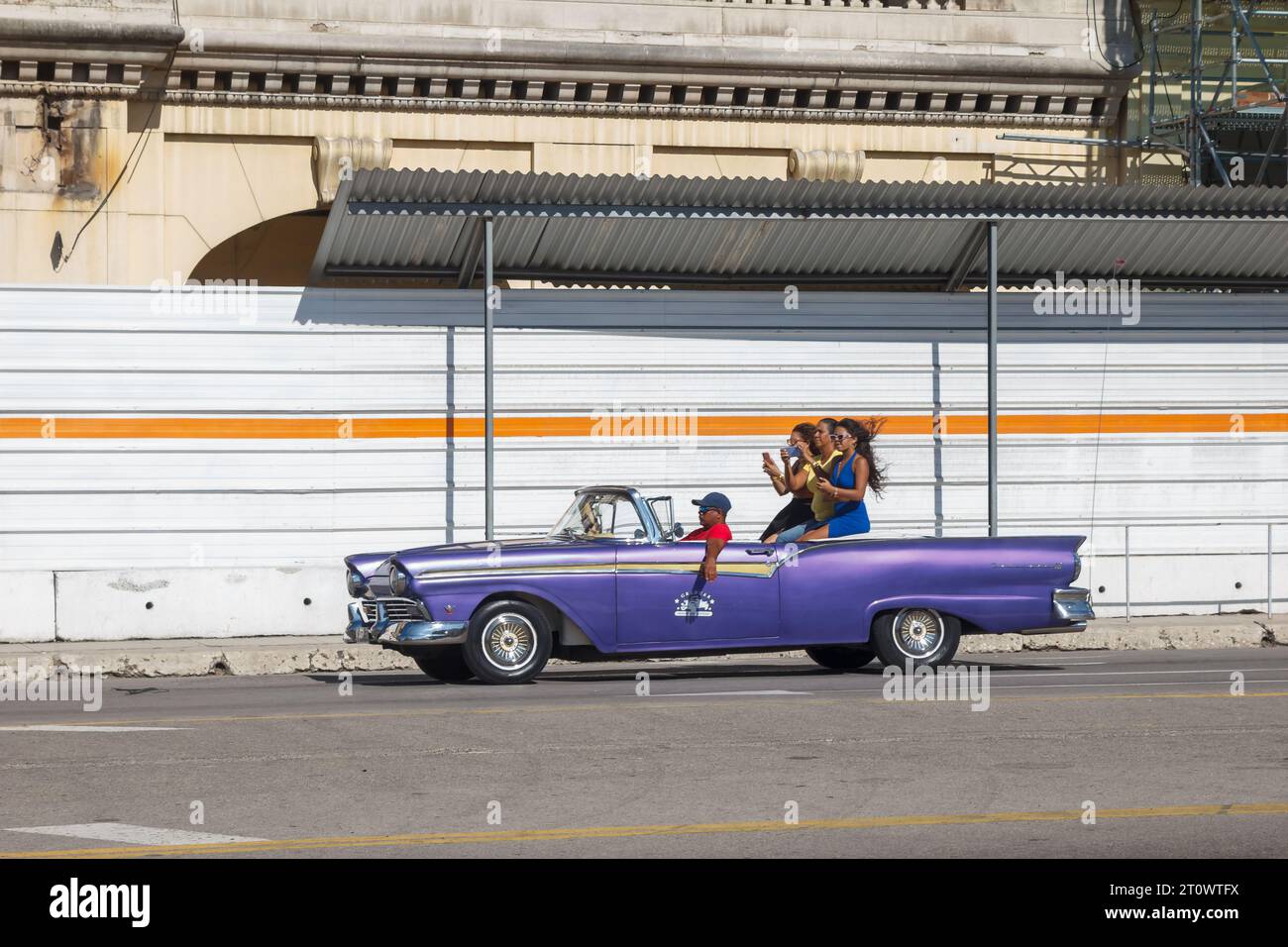 Les femmes de tourisme montent sur une voiture américaine vintage couvrable dans la capitale. En arrière-plan, un ancien bâtiment est en reconstruction ou en revitalisation Banque D'Images
