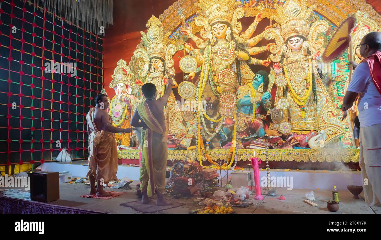 Howrah, Bengale occidental, Inde - 5 octobre 2022 : Hindu Purohis adorant la déesse Durga , dévot avec un grand ventilateur de main la diffusant à l'intérieur de Puja pandal. Banque D'Images