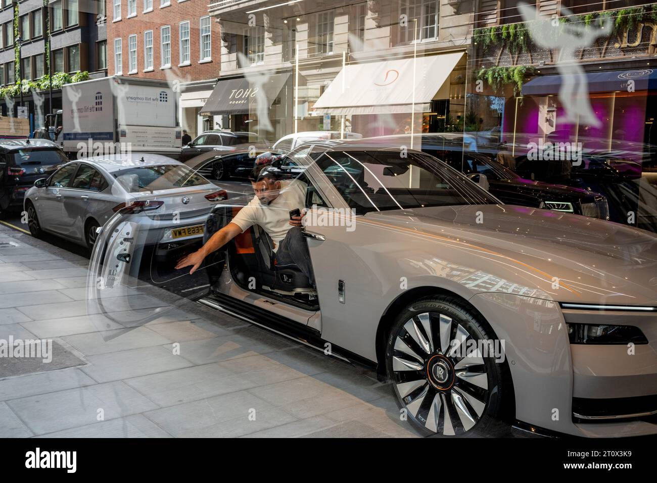 Avec les reflets d'autres voitures garées dans la rue, un acheteur potentiel atteint la porte d'une voiture Rolls-Royce de luxe dans le showroom Mayfair où une voiture est exposée, le 9 octobre 2023, à Londres, en Angleterre. Banque D'Images