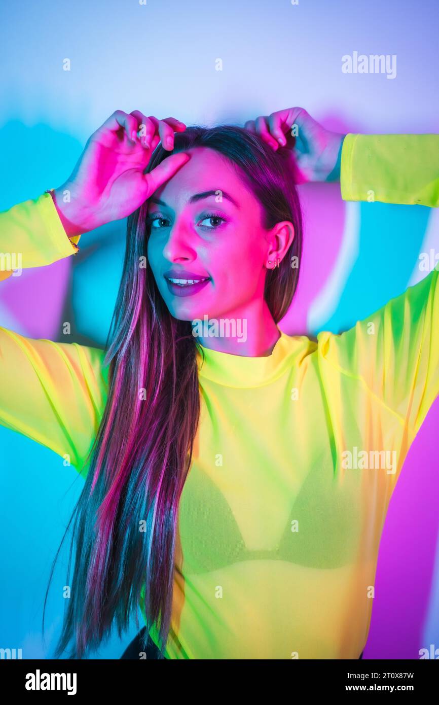 Style de vie de fête dans une boîte de nuit avec des néons bleus roses, portrait d'une jeune fille blonde caucasienne s'amusant dans un t-shirt jaune Banque D'Images