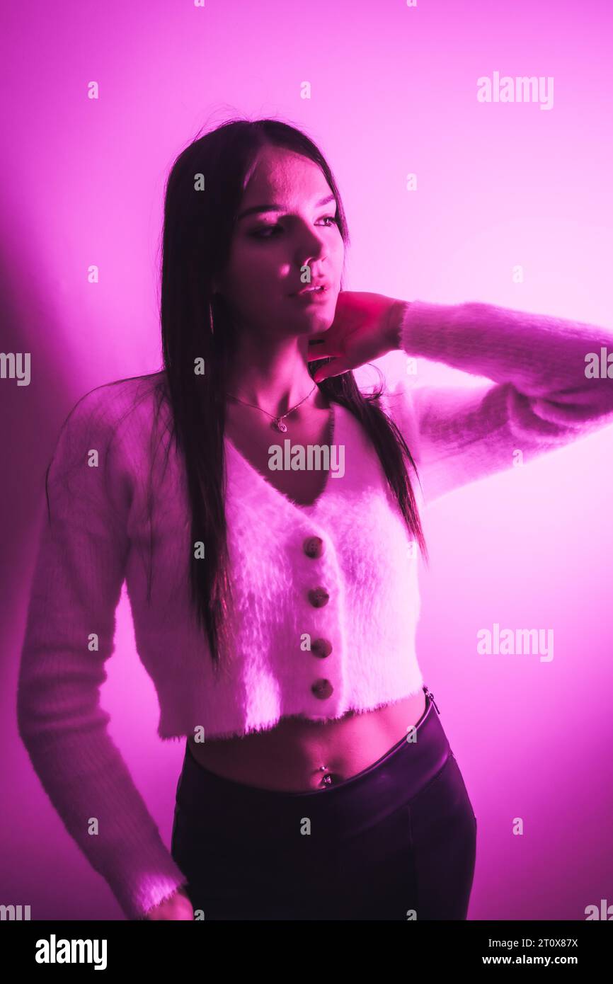 Style de vie de fête dans une boîte de nuit avec des néons roses sur un fond blanc, une jeune femme caucasienne brune dans un pull en laine blanche Banque D'Images