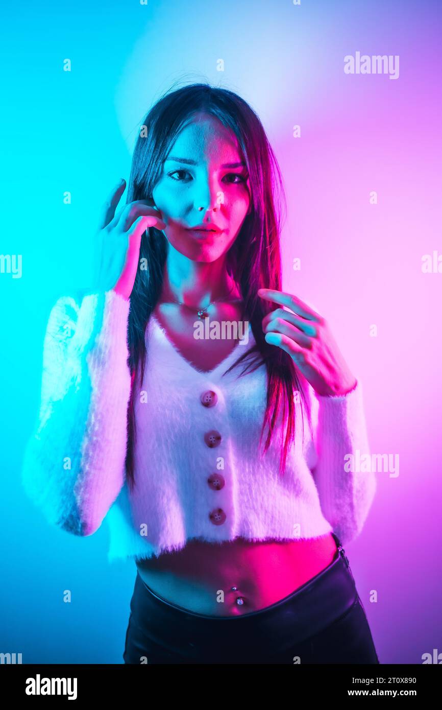Style de vie de fête dans une boîte de nuit avec des néons bleus roses, une jeune femme caucasienne brune dans un pull en laine blanche, photo verticale Banque D'Images