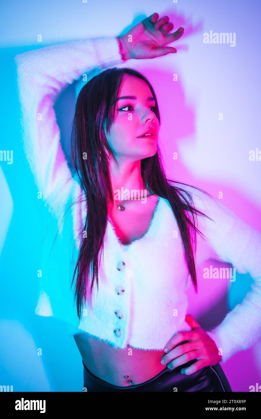 Style de vie de fête dans une boîte de nuit avec des néons bleus roses, portrait d'une jeune femme caucasienne brune dans un pull en laine Banque D'Images