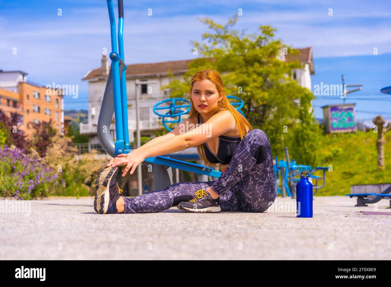 Femme aux cheveux rouges avec des leggings violets et des salopettes noires s'exerçant sur les machines, sport dans la ville Banque D'Images