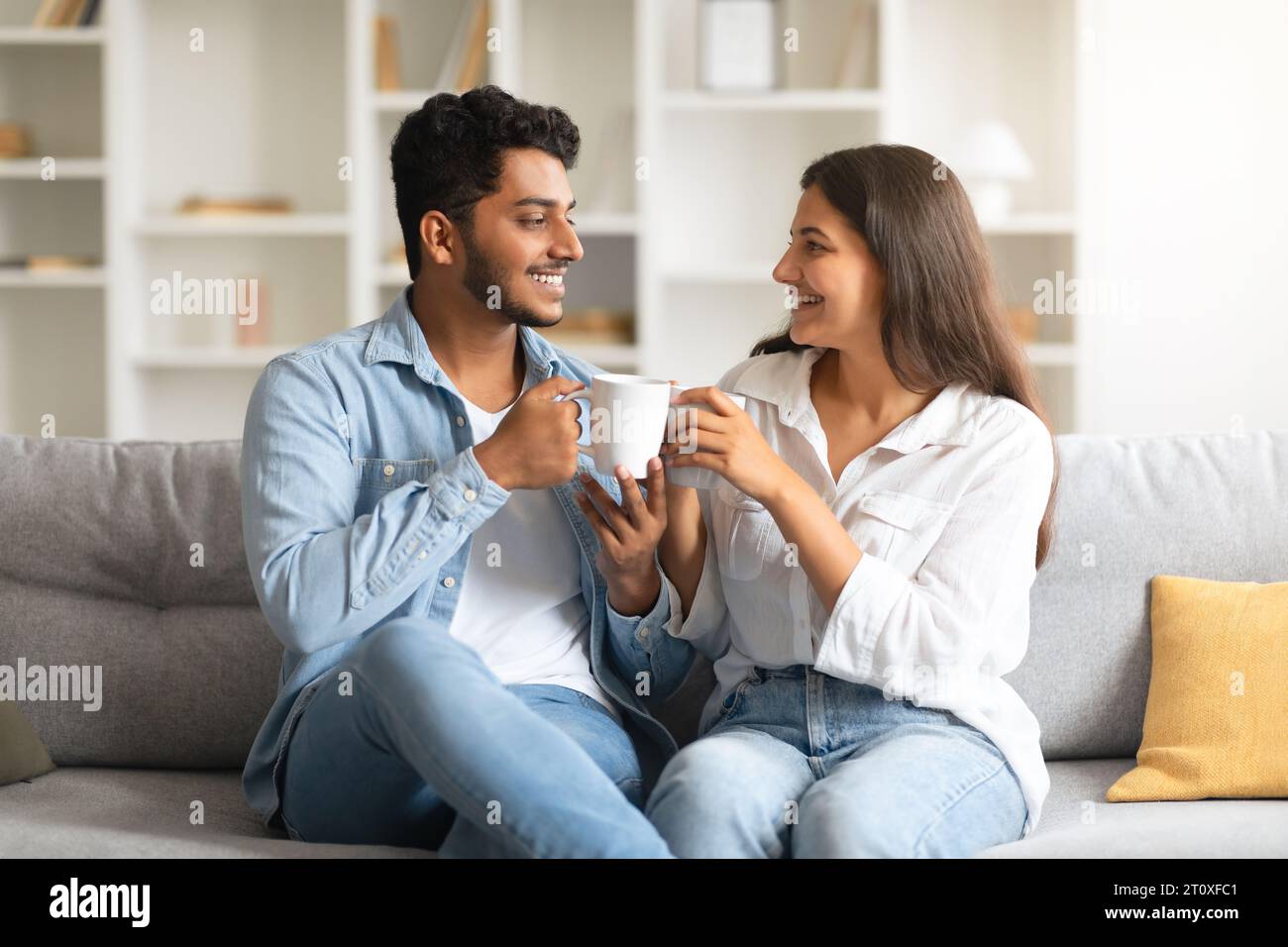 Heureux couple indien parlant et buvant du café, assis sur le canapé Banque D'Images