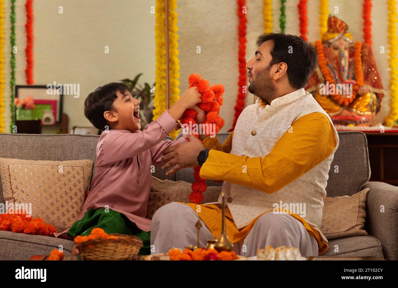 Père et fils garnissant des fleurs ensemble à la maison à l'occasion de Ganesh Chaturthi Banque D'Images