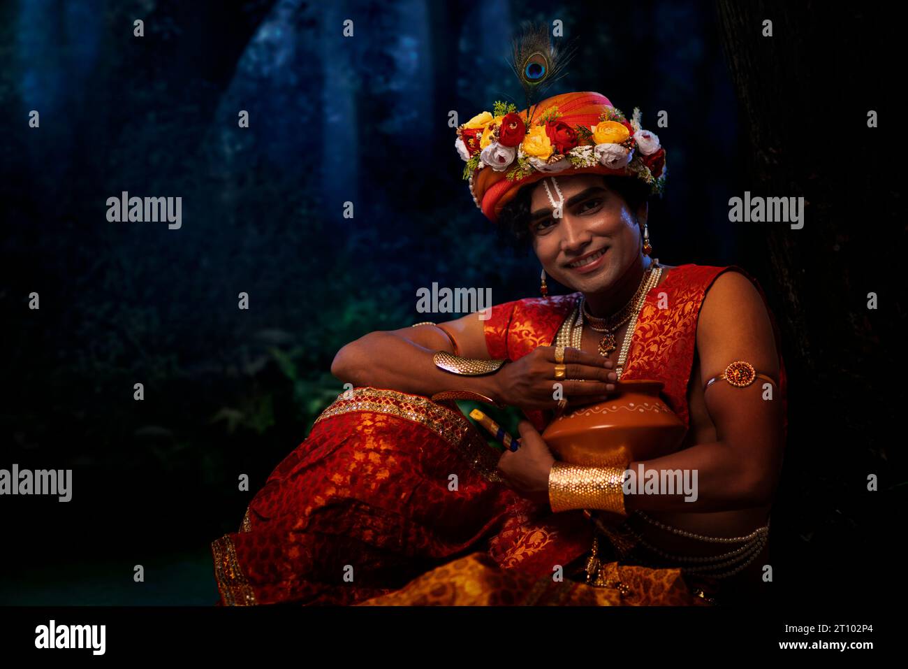 Jeune homme déguisé en Seigneur Krishna et assis avec un pot de beurre à l’occasion de Janmashtami Banque D'Images