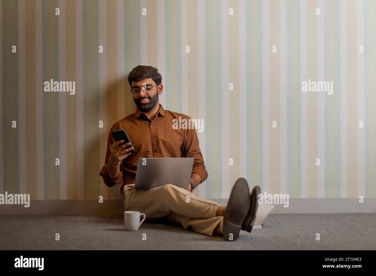 Jeune homme utilisant le téléphone portable tout en travaillant avec un ordinateur portable dans son bureau à domicile Banque D'Images