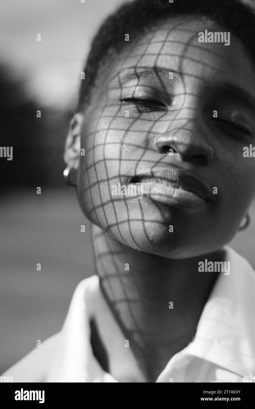 Portrait en noir et blanc d'une jeune femme noire magnifique avec des ombres carrées sur son visage. Banque D'Images
