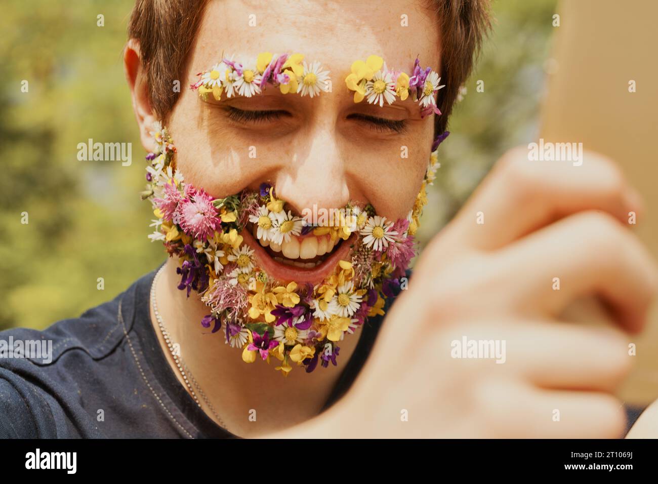 Entouré par l'environnement, un mâle avec une barbe florale unique et des sourcils interagit avec son mobile. Il savoure un environnement paisible, mais reste Banque D'Images