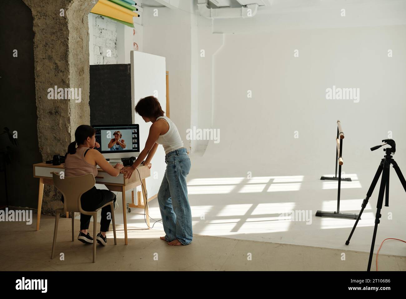 Deux jeunes femmes interculturelles en vêtements décontractés discutant de nouvelles prises de vue sur l'écran d'ordinateur après une séance photo alors que l'une d'entre elles était assise sur une chaise Banque D'Images