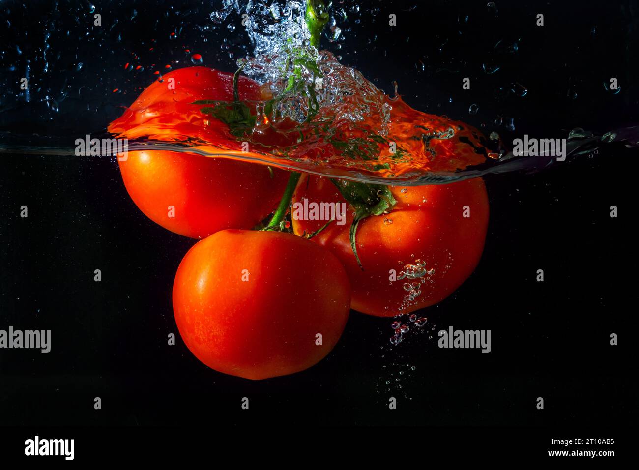 Tomate rouge fraîche tombant dans l'eau avec des éclaboussures d'eau et des bulles d'air isolées sur fond noir. Banque D'Images