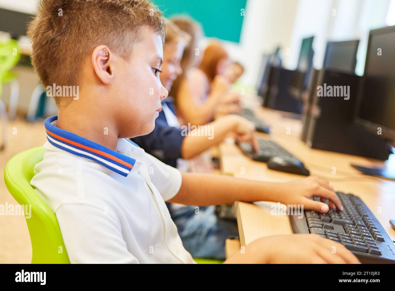 Vue latérale d'un écolier élémentaire utilisant un ordinateur assis sur une chaise en classe Banque D'Images
