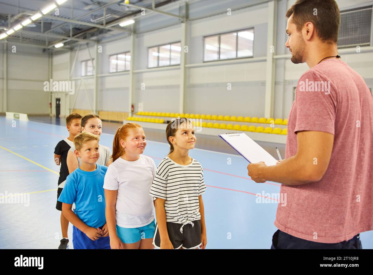 Enseignant de sexe masculin prenant l'examen physique des élèves du primaire debout dans la queue pendant le cours de gym Banque D'Images
