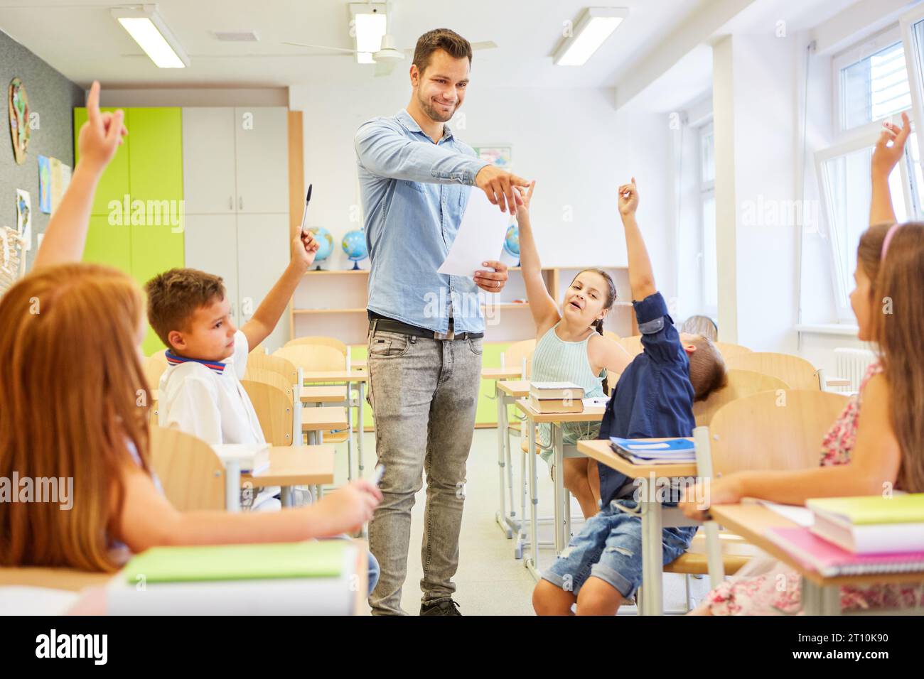 Enseignant souriant pointant du doigt une étudiante assise avec la main levée dans la salle de classe Banque D'Images