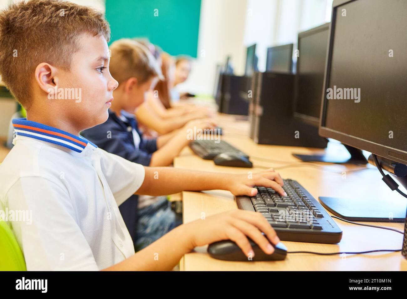 Vue latérale d'un écolier regardant l'écran d'ordinateur assis au bureau dans la salle de classe Banque D'Images