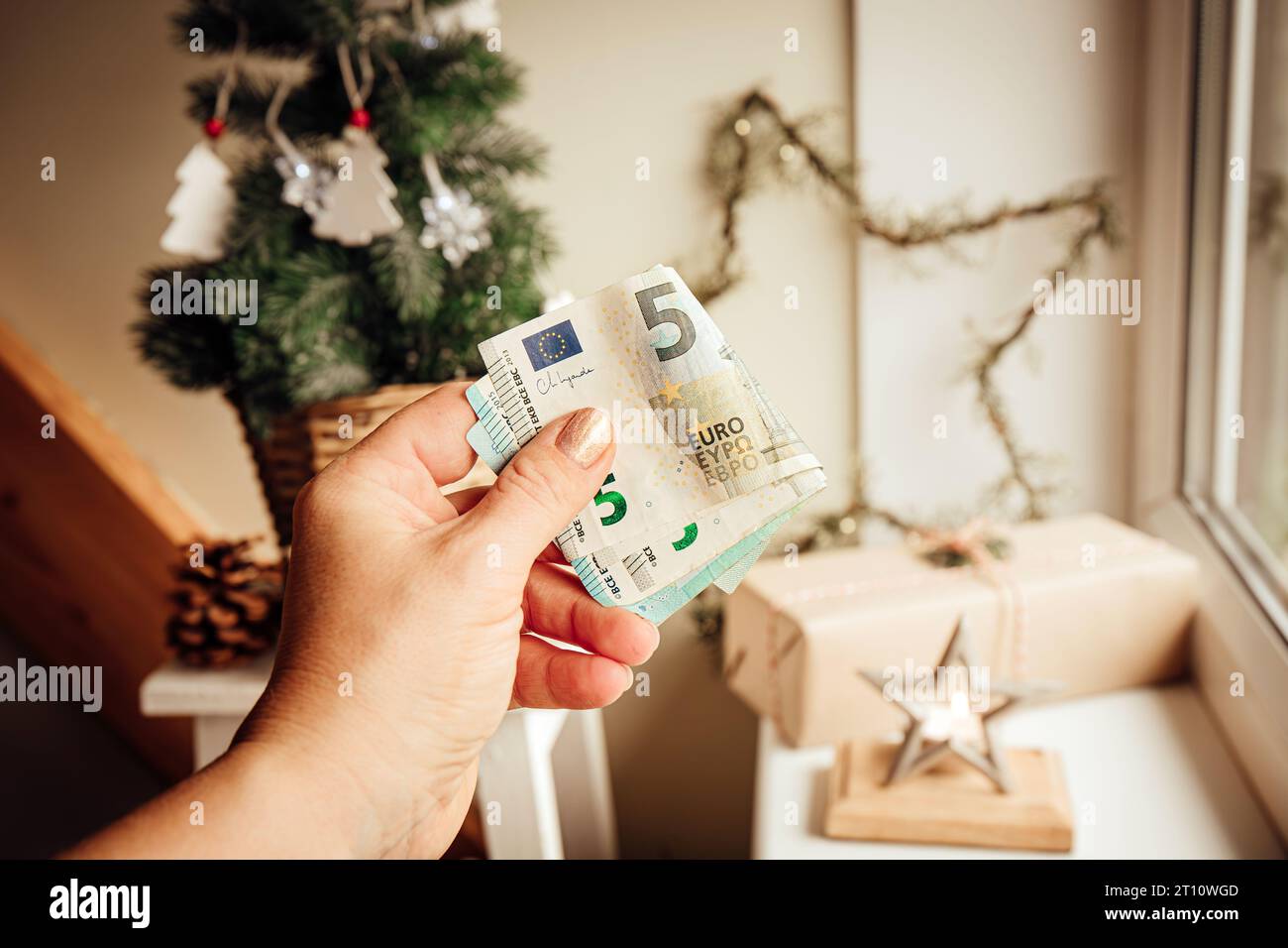 Concept de budget et de finances de Noël. Main de femme tenant de l'argent contre l'arbre de Noël et des ornements à la maison. Banque D'Images