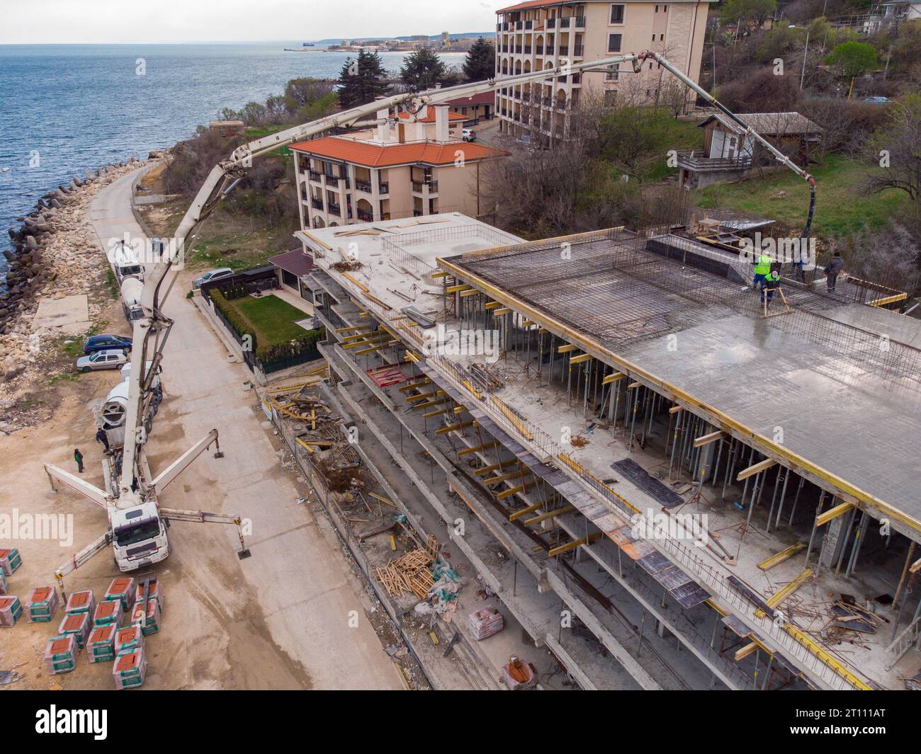 Couler du ciment de béton sur le toit d'un bâtiment résidentiel en construction à l'aide d'une machine de camion de pompe à béton avec flèche haute pour alimenter le mixtur Banque D'Images