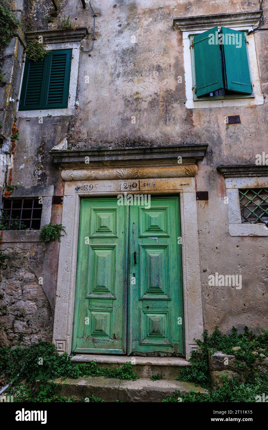 maison abandonnée aux murs en pierre avec porte en bois vert et volets sur le quai du port de zlarin Banque D'Images