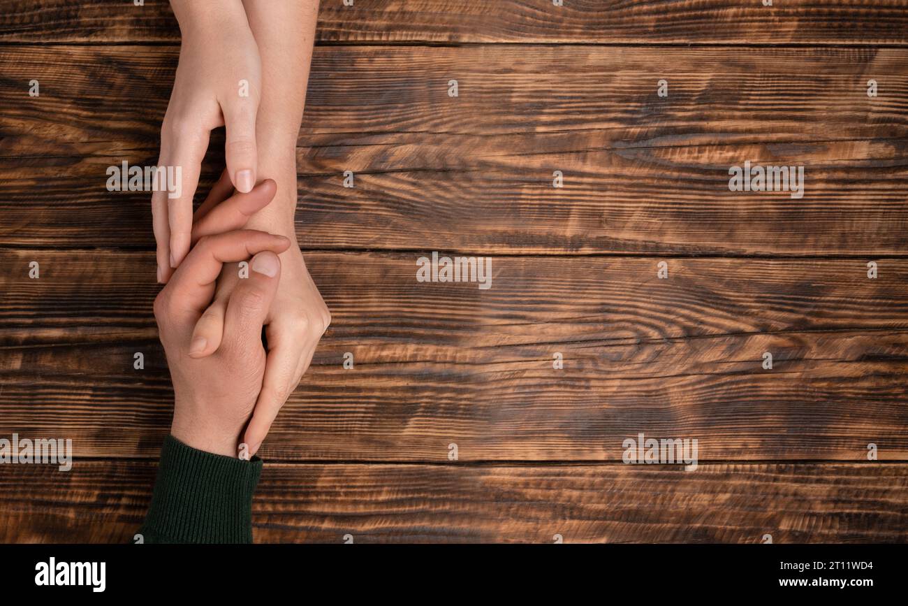 Concept d'amour et de famille. Les mains féminines embrassent la main masculine sur fond en bois brun avec espace de copie. La manifestation de l'affection et de la confiance. Fête de la famille, Banque D'Images