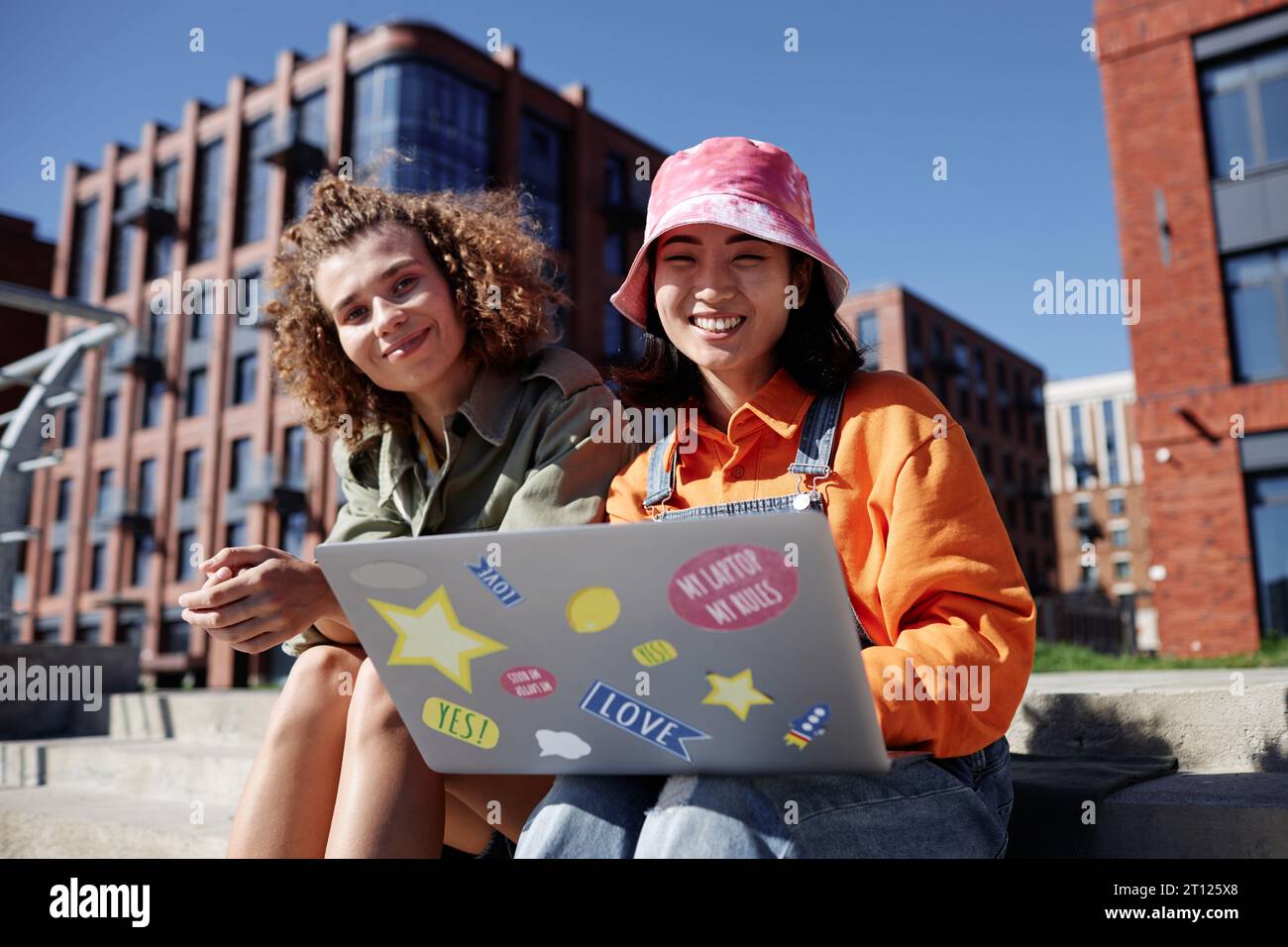 Portrait coloré de deux jeunes femmes utilisant l'ordinateur à l'extérieur tout en étant assis sur des escaliers en béton dans la ville Banque D'Images