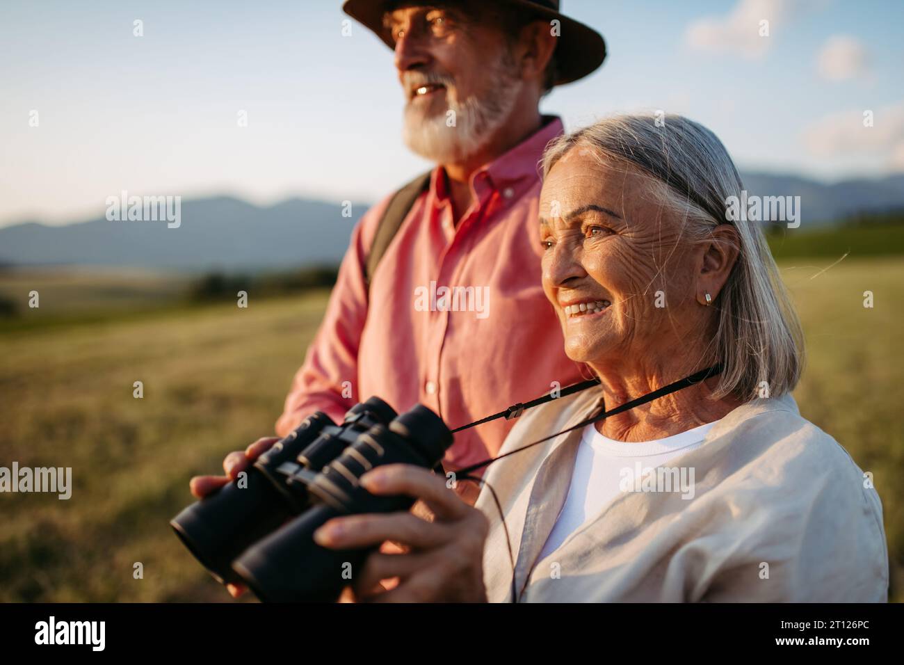 Portrait d'une femme âgée regardant à travers des jumelles. Des conjoints âgés vont cueillir des champignons. Banque D'Images