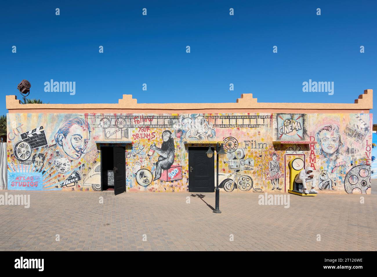 Ouarzazate, Maroc - 10 octobre 2023 : mur peint avec les visages d'artistes et différents graffitis et un jeune garçon assis sur une échelle. Banque D'Images