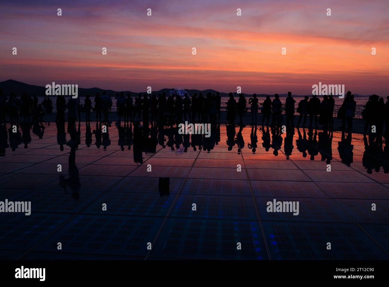 les foules se rassemblent autour d'un saxophoniste solo au coucher du soleil reflété dans les panneaux solaires de la salutation à l'installation du soleil au coucher du soleil à zadar croatie Banque D'Images