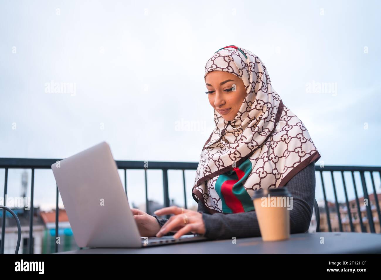 Fille arabe dans un voile blanc à l'ordinateur sur la terrasse d'un magasin de café, faisant un appel vidéo. Jeune homme arabe moderne avec les nouvelles technologies Banque D'Images