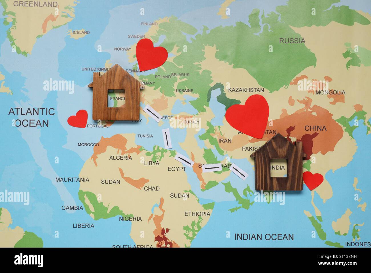 Coeurs de papier et marques entre les modèles de maison en bois sur la carte du monde symbolisant la connexion dans la relation à longue distance, la pose plate Banque D'Images