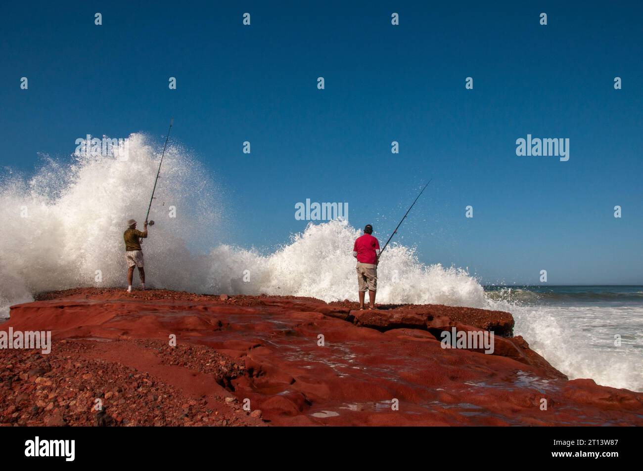 Deux hommes pêchant à Legzira Plage. Un sur le point d'être attrapé par des vagues venant de l'Atlantique. Nov 2009 Banque D'Images
